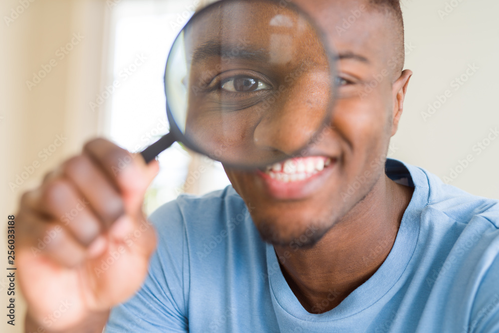 Young african man looking through magnifying glass Young african man looking through magnifying glass