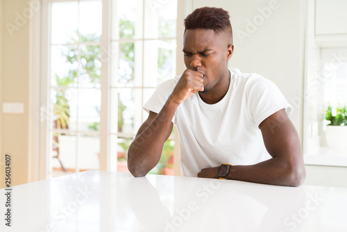 Handsome african american man on white table at home feeling unwell and coughing as symptom for cold or bronchitis. Healthcare concept.