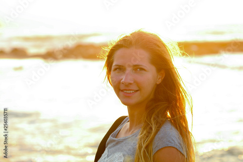 Candid portrait of young woman by the sea at sunset, strong sun backlight, background overexposed intentionally for atmosphere photo