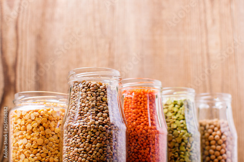 Different legumes in glass jars on a wooden background
