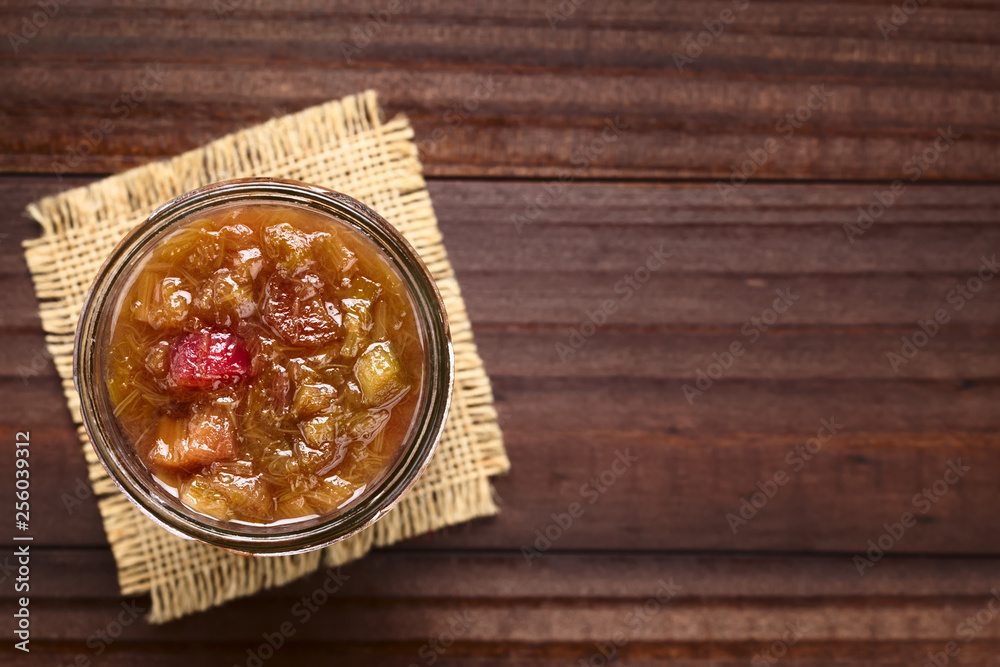 Fototapeta premium Homemade rhubarb jam in jar photographed overhead on dark wood (Selective Focus, Focus on the jam)