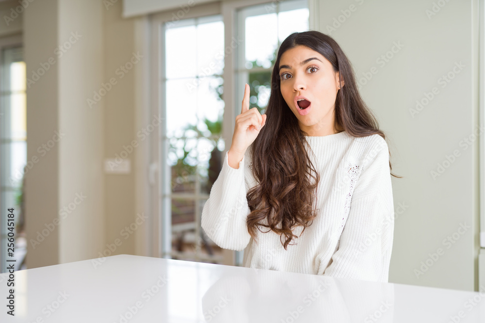 Young beautiful woman at home on white table pointing finger up with successful idea. Exited and happy. Number one. Young beautiful woman at home on white table pointing finger up with successful idea. Exited and happy. Number one.