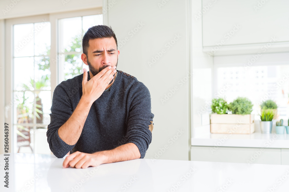 Handsome hispanic man wearing casual sweater at home bored yawning tired covering mouth with hand. Restless and sleepiness.