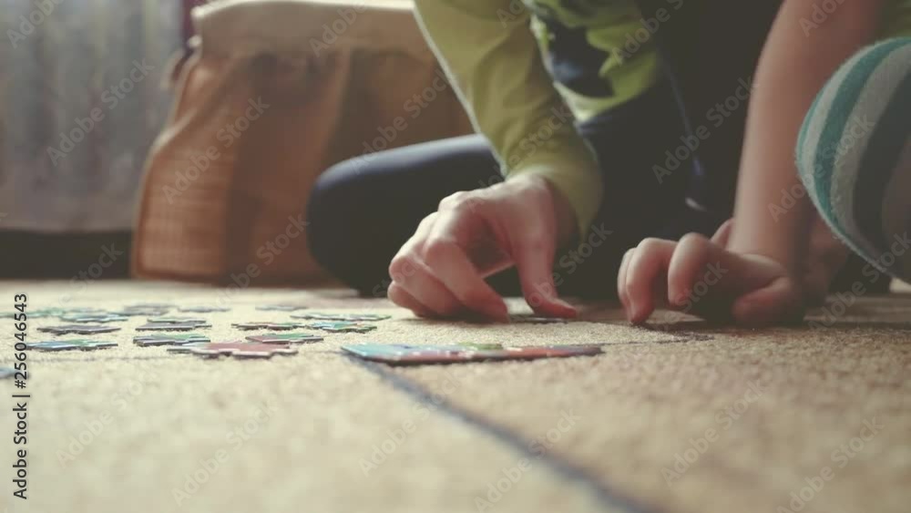 Mother and daughter doing a puzzle together in the light living room. Close-up of mom's and baby girl's hands in scene and mommy showing daughter place for puzzle detail.