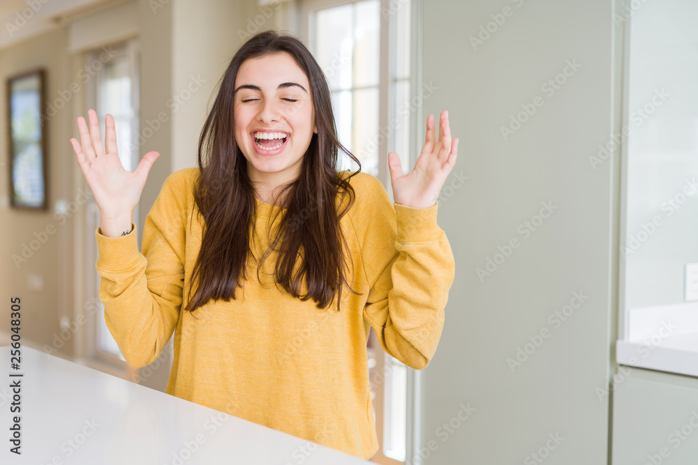 Beautiful young woman wearing yellow sweater celebrating mad and crazy for success with arms raised and closed eyes screaming excited. Winner concept Beautiful young woman wearing yellow sweater celebrating mad and crazy for success with arms raised and closed eyes screaming excited. Winner concept