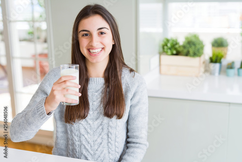 Beautiful young woman drinking a glass of fresh milk with a happy face standing and smiling with a confident smile showing teeth