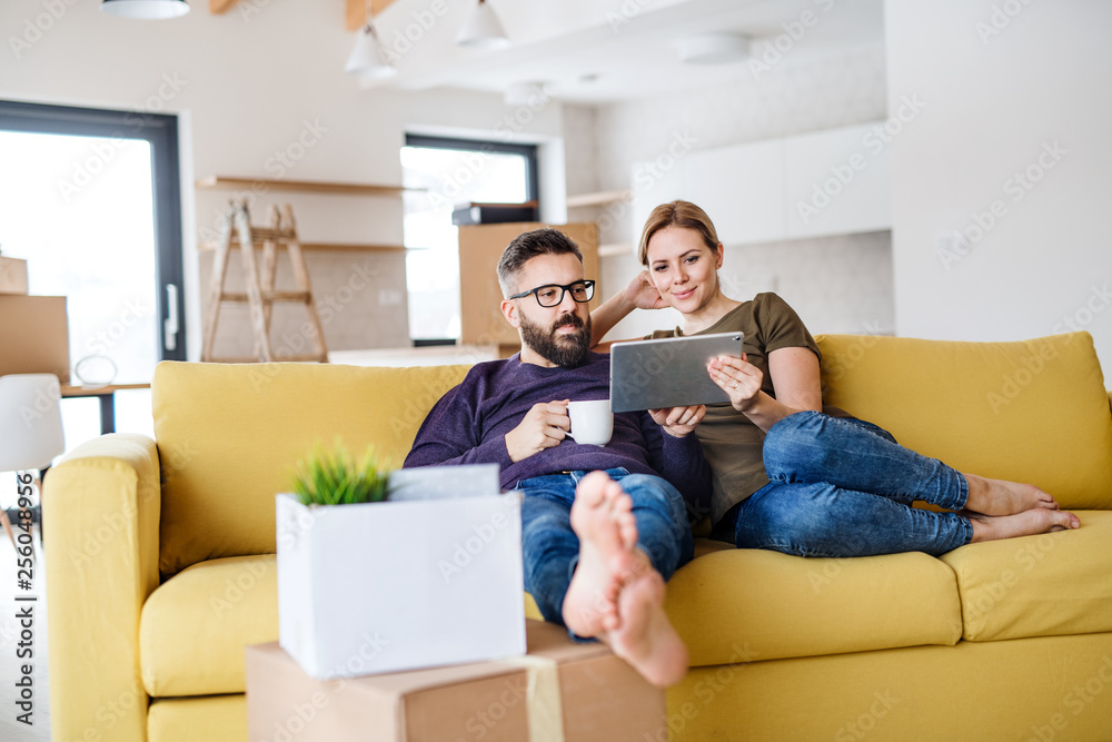 A young couple with tablet and coffee sitting on sofa, moving in new home. A young couple with tablet and coffee sitting on sofa, moving in new home.