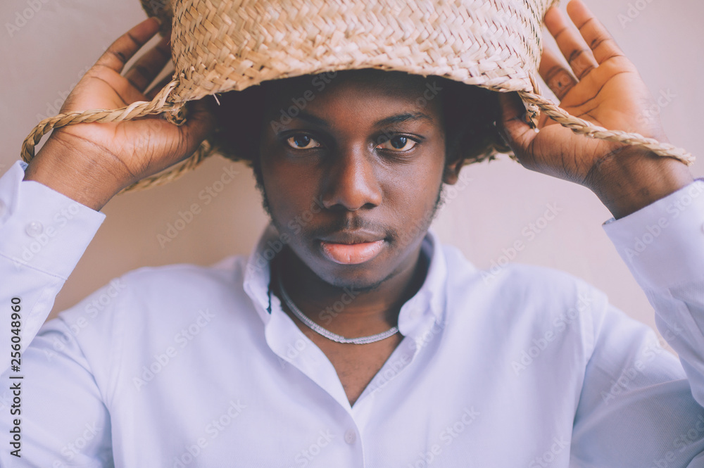 Closeup lifestyle portrait of strange young african black man holding straw basket above his head on textured wall background and looking at camera. Dark-skinned nigerian boy indoor funny portrait. Stock Photo | Closeup lifestyle portrait of strange young african black man holding straw basket above his head on textured wall background and looking at camera. Dark-skinned nigerian boy indoor funny portrait. Stock Photo |