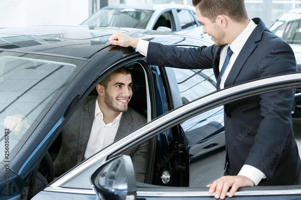 This is the one. Horizontal portrait of a handsome young businessman sitting in the car and talking to a car dealer standing near This is the one. Horizontal portrait of a handsome young businessman sitting in the car and talking to a car dealer standing near