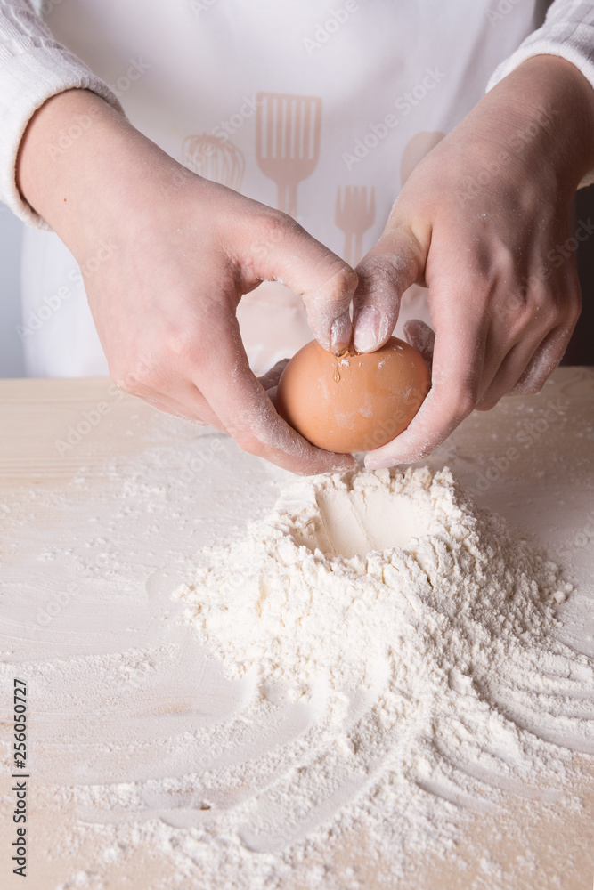 Young woman breaks egg above white flour to make dough for italian pasta Young woman breaks egg above white flour to make dough for italian pasta