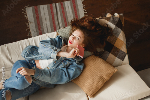 Cute young woman in jeans clothes lying in sofa with pink diary. photo