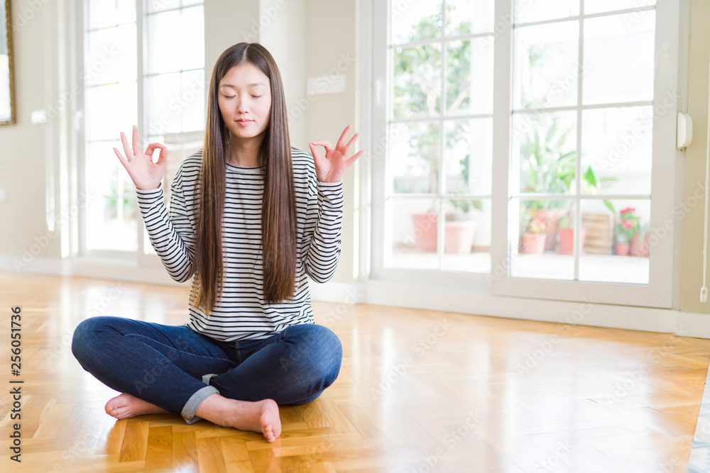 Beautiful Asian woman sitting barefoot on the floor at home relax and smiling with eyes closed doing meditation gesture with fingers. Yoga concept. Beautiful Asian woman sitting barefoot on the floor at home relax and smiling with eyes closed doing meditation gesture with fingers. Yoga concept.