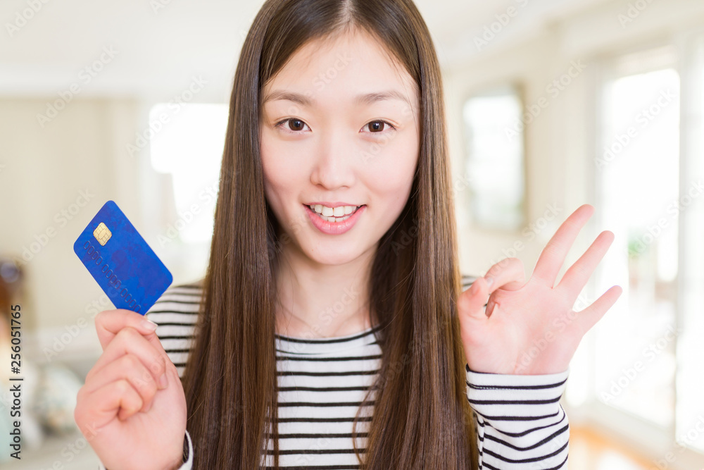 Beautiful Asian woman holding credit card doing ok sign with fingers, excellent symbol Beautiful Asian woman holding credit card doing ok sign with fingers, excellent symbol