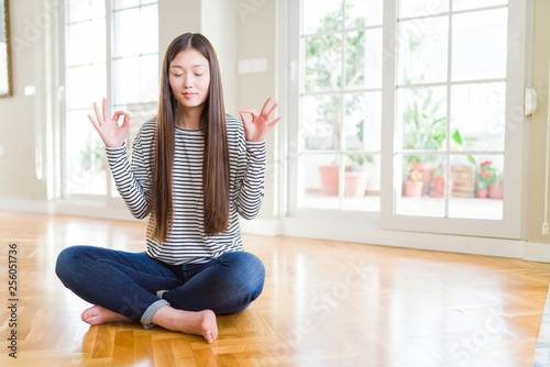 Free Download Beautiful Asian woman sitting barefoot on the floor at home relax and smiling with eyes closed doing meditation gesture with fingers. Yoga concept. - GFXLoad