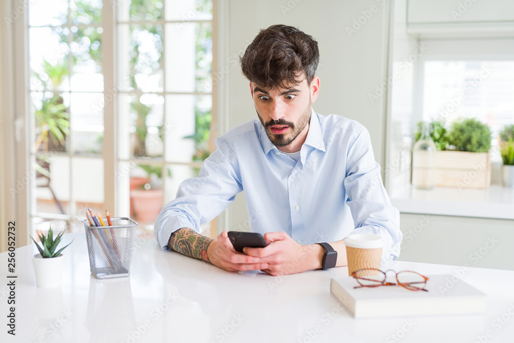 Young business man using smartphone sending a message scared in shock with a surprise face, afraid and excited with fear expression Young business man using smartphone sending a message scared in shock with a surprise face, afraid and excited with fear expression