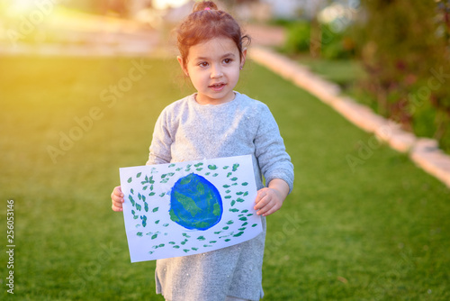 Portrait of the cute little girl holding the drawing earth globe outdoor sunny day. Child drawng a picture of earth.Earth day, plastic free and zero waste concept. photo