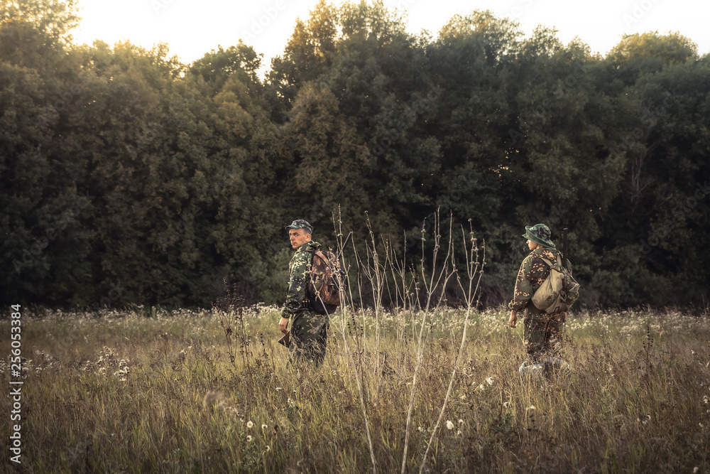 Hunting hunters standing in rural field nearby forest at sunset during hunting season Hunting hunters standing in rural field nearby forest at sunset during hunting season