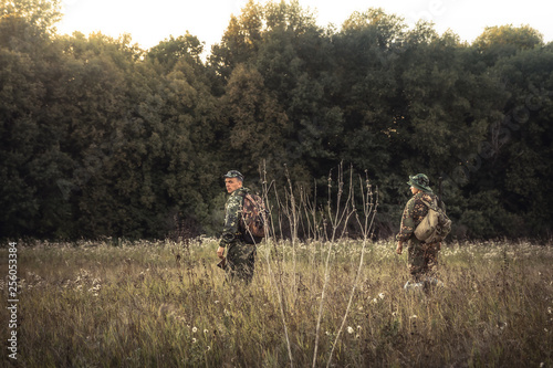 Hunting hunters standing in rural field nearby forest at sunset during hunting season