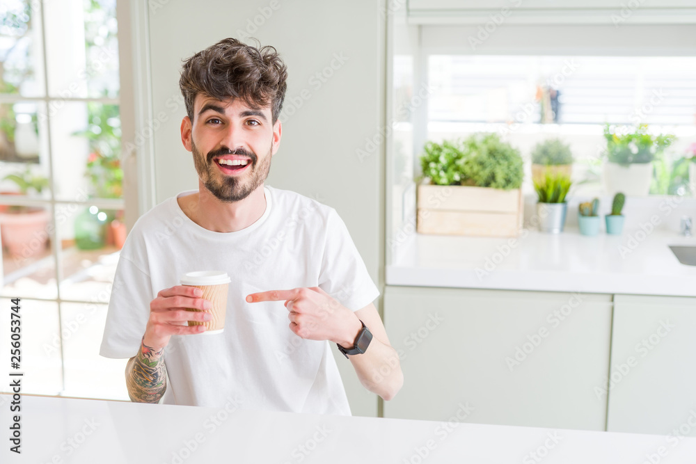Young man drinking a coffee in a paper cup in the morning very happy pointing with hand and finger Young man drinking a coffee in a paper cup in the morning very happy pointing with hand and finger