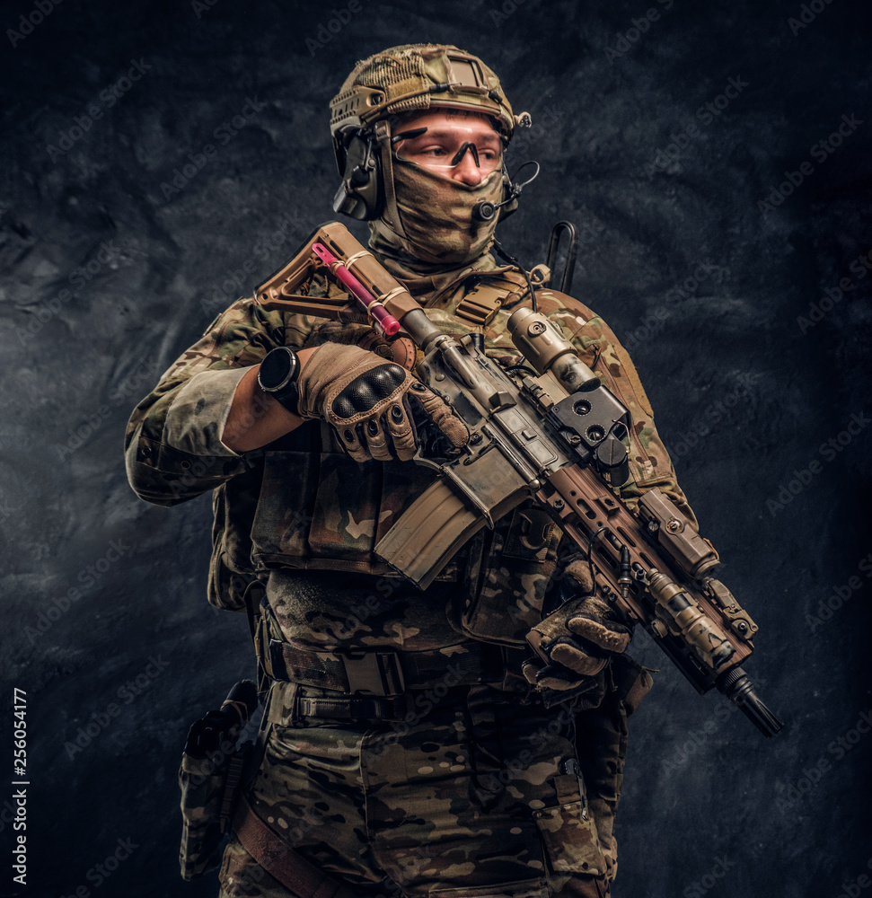 The elite unit, special forces soldier in camouflage uniform holding an assault rifle with a laser sight. Studio photo against a dark wall The elite unit, special forces soldier in camouflage uniform holding an assault rifle with a laser sight. Studio photo against a dark wall
