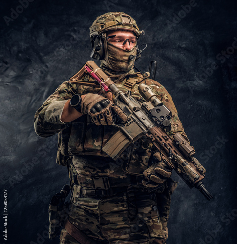 The elite unit, special forces soldier in camouflage uniform holding an assault rifle with a laser sight. Studio photo against a dark wall