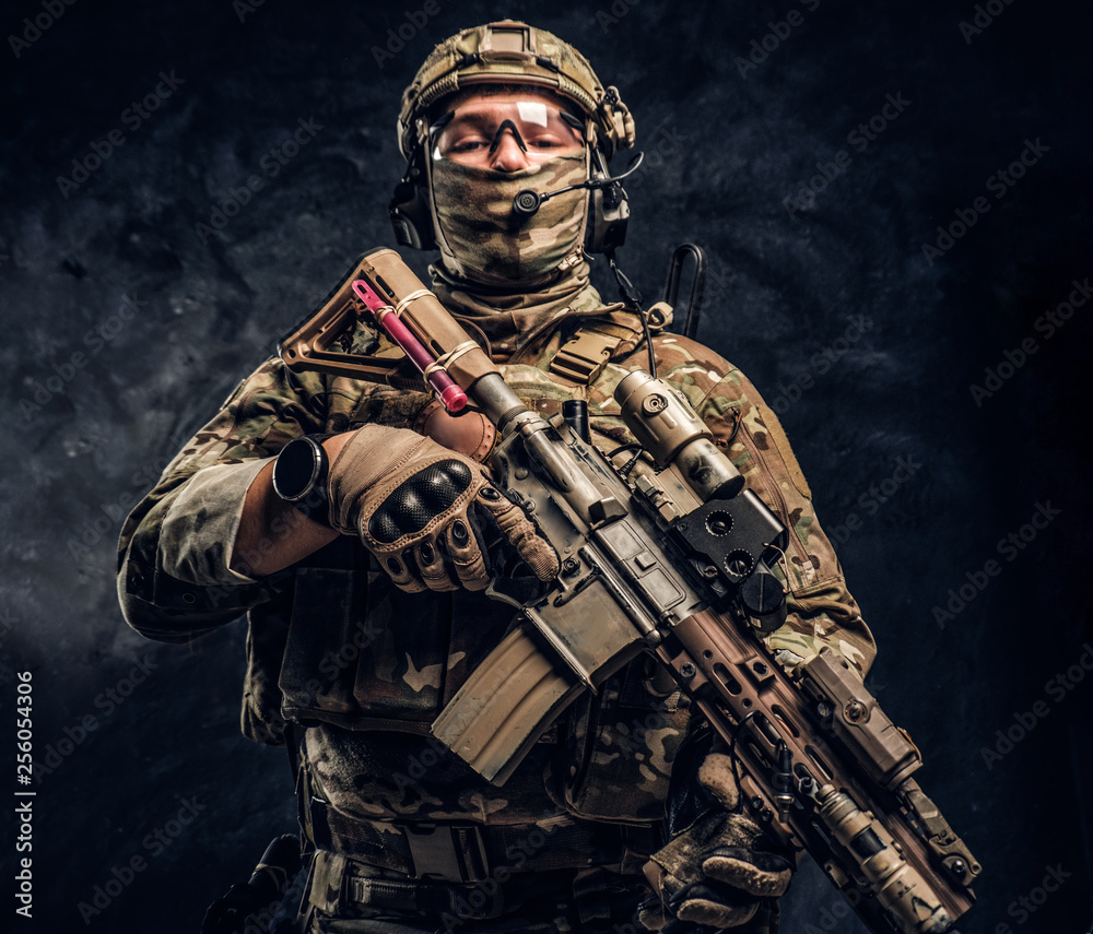 Naklejka premium The elite unit, special forces soldier in camouflage uniform holding an assault rifle with a laser sight. Studio photo against a dark wall