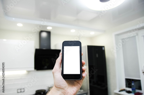 Smartphone with white screen in the kitchen, smart home system, concept of energy saving and technological lighting control.