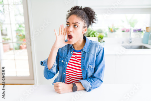 Beautiful young african american woman with afro hair wearing casual denim jacket shouting and screaming loud to side with hand on mouth. Communication concept.