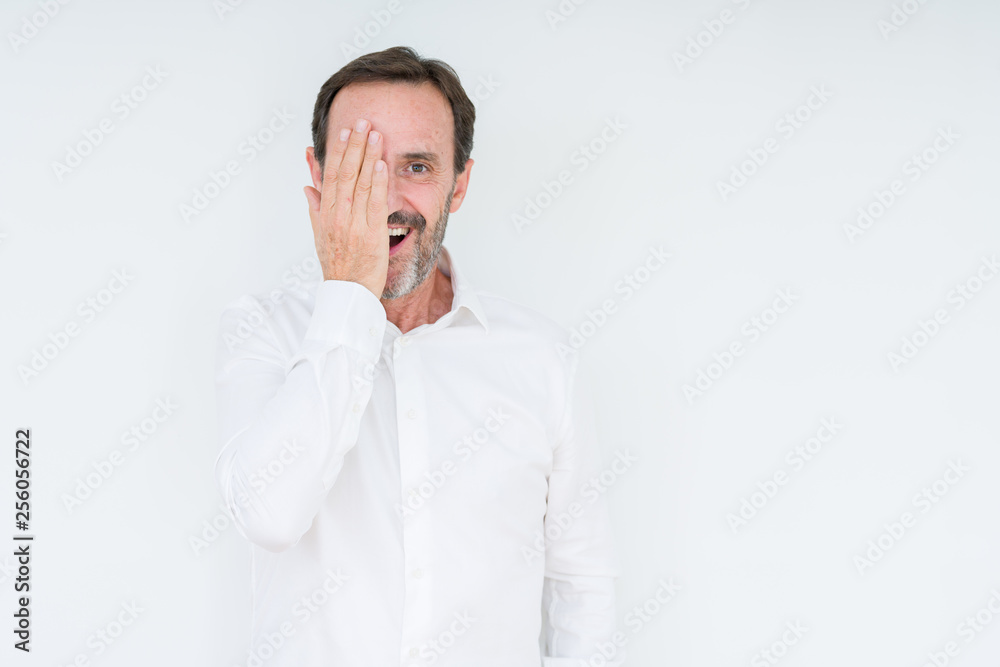 Elegant senior man over isolated background covering one eye with hand with confident smile on face and surprise emotion. Elegant senior man over isolated background covering one eye with hand with confident smile on face and surprise emotion.