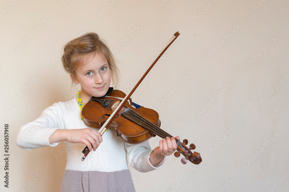 Cute little girl in a beautiful dress playing violin. Joyful and happy emotions. Training. Education. School. Aesthetic training. Portrait of a young girl playing violin on light background Cute little girl in a beautiful dress playing violin. Joyful and happy emotions. Training. Education. School. Aesthetic training. Portrait of a young girl playing violin on light background