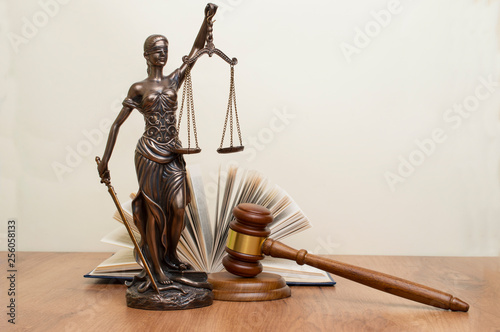 statue of justice, judge's hammer behind books on a wooden table