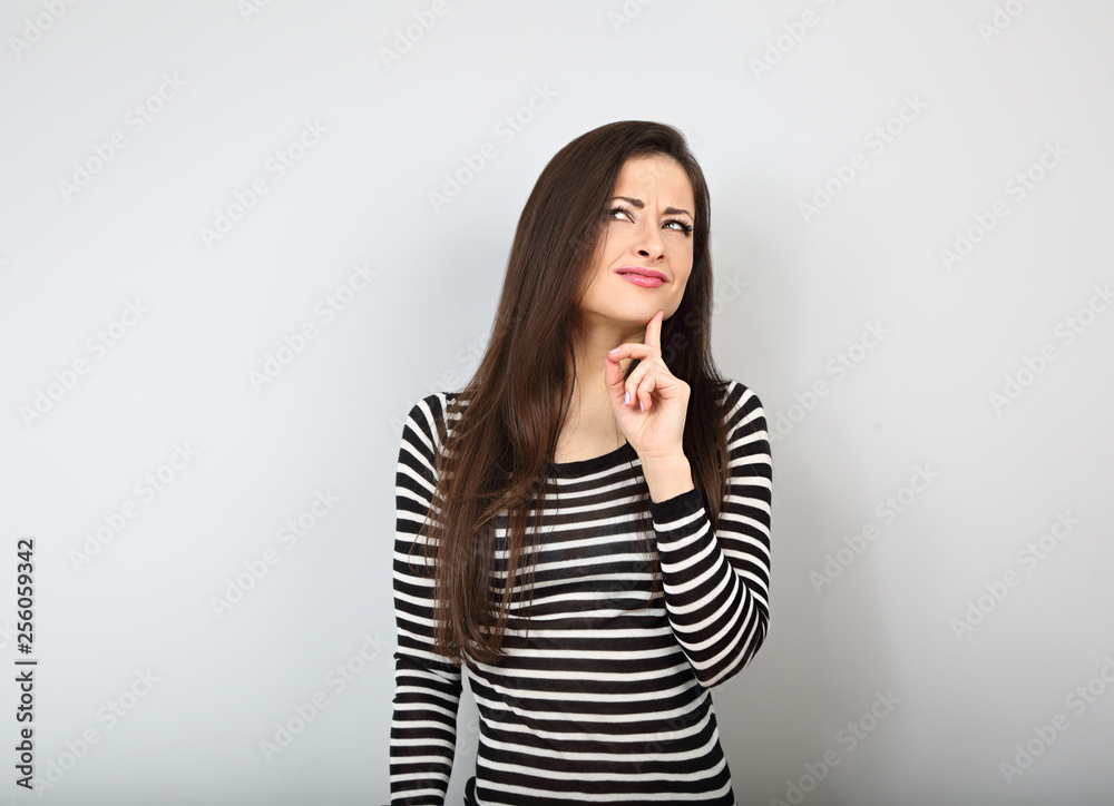 Beautiful uncertain woman with finger under the face thinking and looking up in casual shirt and long hair.