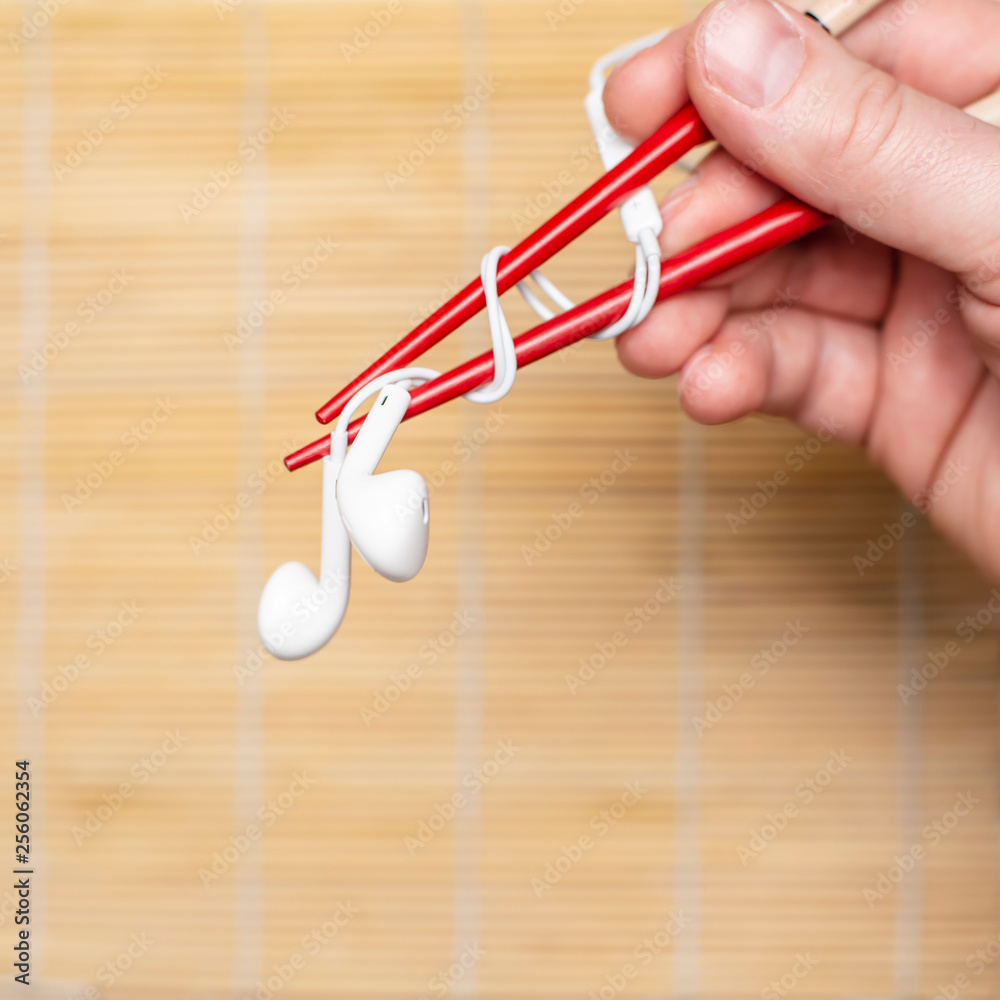 Hand is holding a headphones using chopsticks on a blurred background. Concept of musical taste. Hand is holding a headphones using chopsticks on a blurred background. Concept of musical taste.