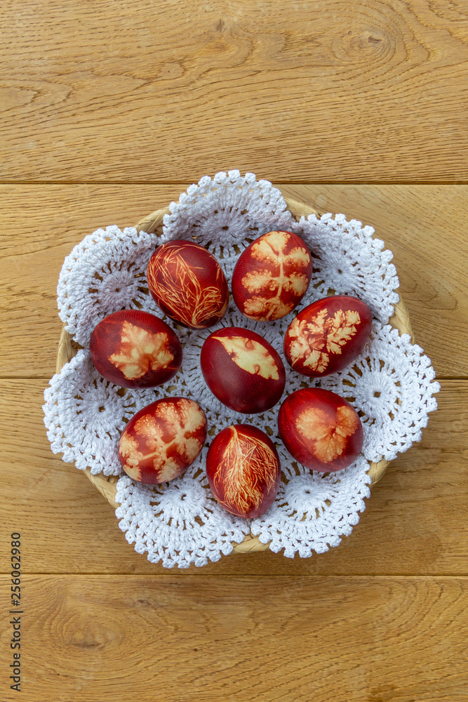 Easter eggs dyed with onion peels with a pattern of plants and leaves in a basket on a white lace doily, on a wooden background. Top view, closeup, vertical photo. Symbol of Christian tradition.