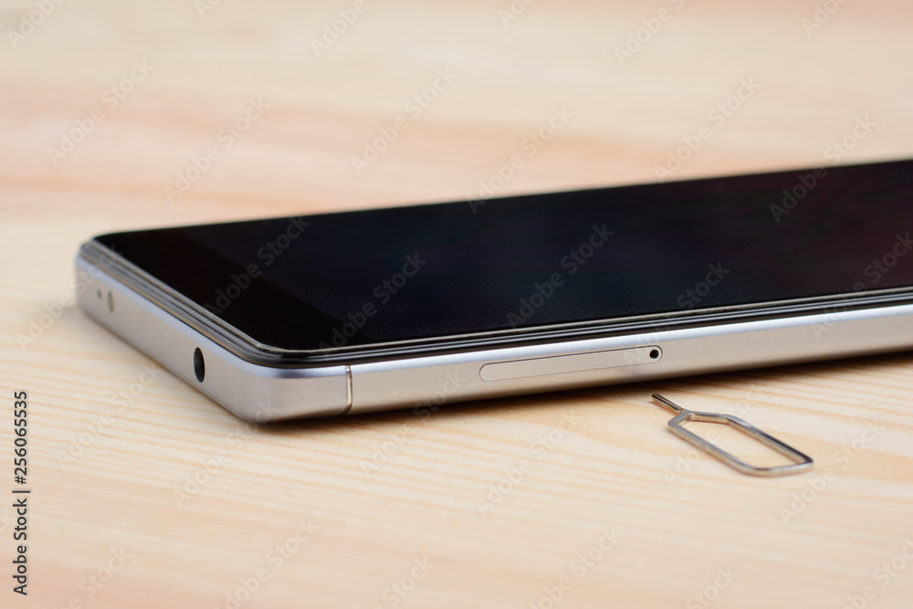 Removal SIM card tray out from the mobile phone near a modern smartphone on a wooden table Removal SIM card tray out from the mobile phone near a modern smartphone on a wooden table