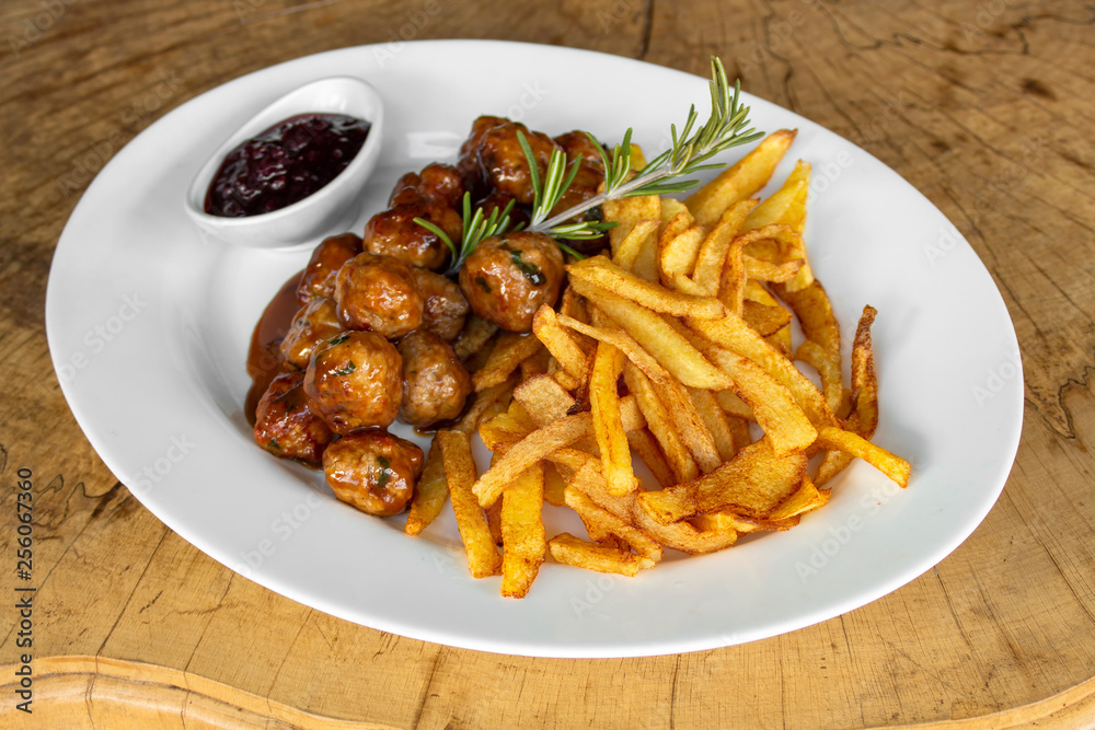 Mini meatballs with Gravy sauce and fried potatoes. Garnished with cranberry jam and rosemary sprig.
