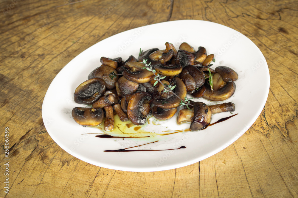 Mushrooms roasted with butter. With thyme and rosemary. In a white plate on a wooden background. Mushrooms roasted with butter. With thyme and rosemary. In a white plate on a wooden background.