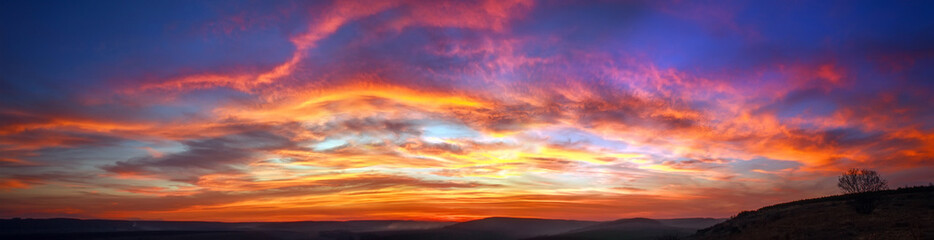 Fototapete Sonnenuntergang Panorama bunter herrlicher Sonnenuntergang auf dem Land über Hügeln und Feldern, Schönheitsnaturhintergrund  © okostia