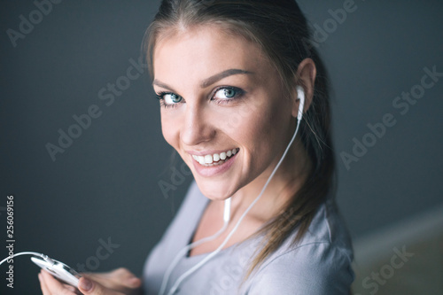 Happy young  smiling woman in earphones is listening to music with smart phone.