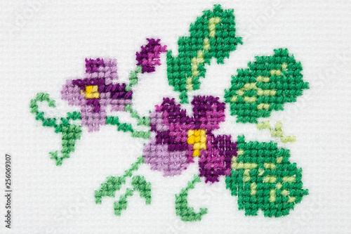 Violet flower embroidered with a cross on textile canvas