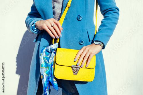 Young woman holding stylish handbag and wearing trendy blue coat. Spring female clothes and accessories. Fashion