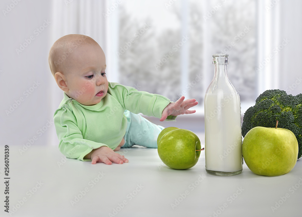Fototapeta premium Small child reaches for a fresh green apple on a white table