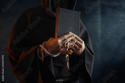Medieval monk holds book and wooden cross in hands