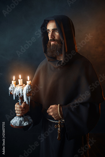 Obraz na plátne Medieval monk in robe holds a candlestick in hands