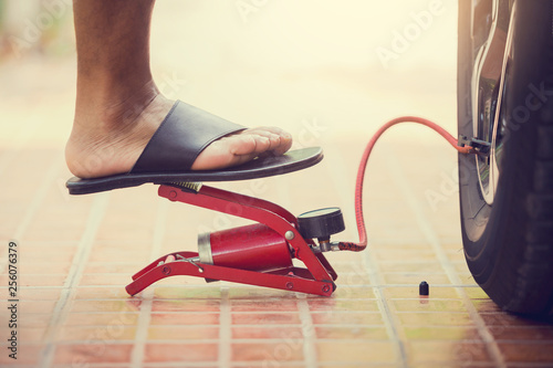 man Inflating car tyre with foot pump, man put black sandals Inflating car tyre with red foot pump in garage in the house, the concept of checking a car before traveling photo