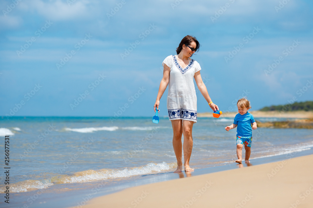 Young mother and her cute little baby girl playing on a beautiful tropical beach
