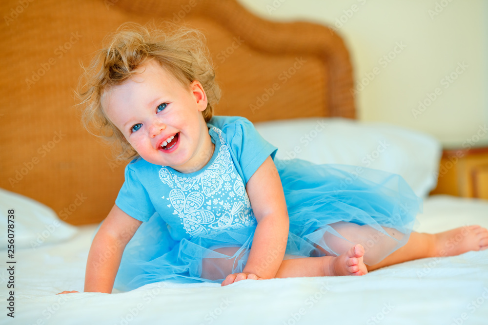 Lovely happy blonde toddler girl sitting on a bed Lovely happy blonde toddler girl sitting on a bed
