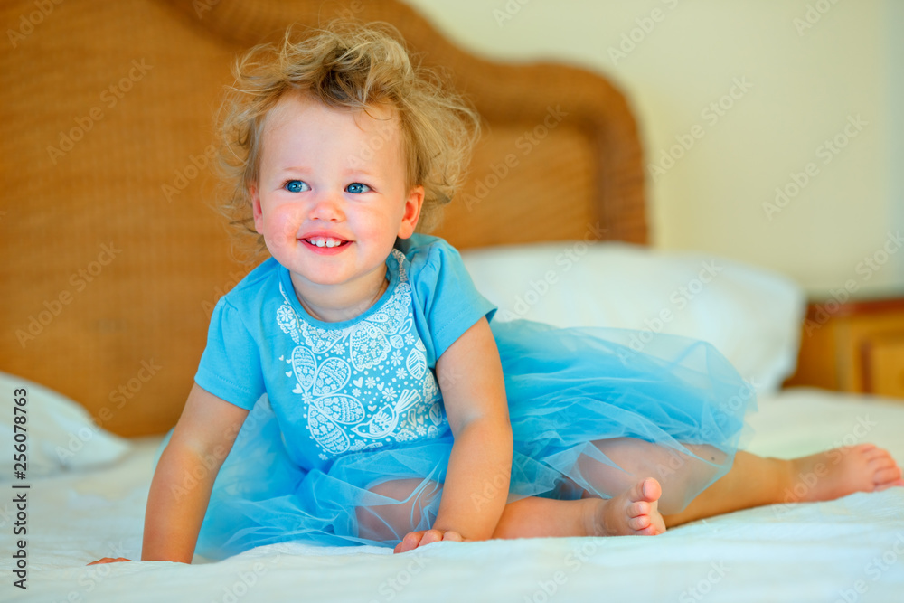Lovely happy blonde toddler girl sitting on a bed Lovely happy blonde toddler girl sitting on a bed