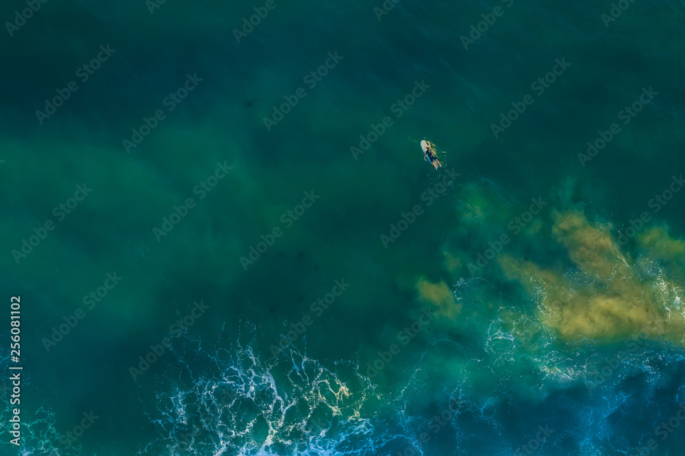 Lonely surfer lying on surfboard in vast ocean - aerial view with copy space