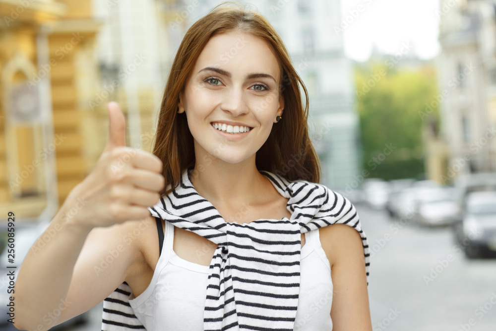 Great! Beautiful young female shows thumbs up smiling looking to the camera